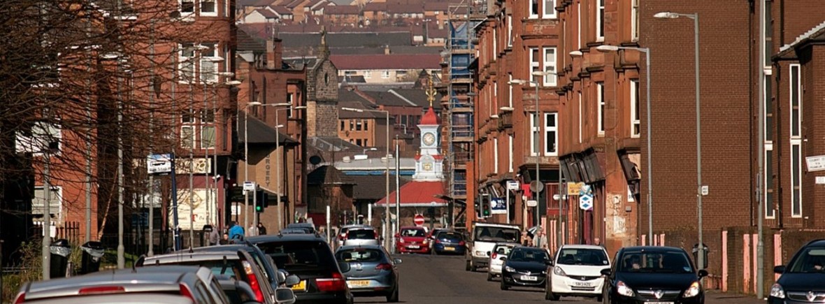 Street in the Bridgeton and Dalmarnock neighbourhood with red brick tenements on either side and cars on the road