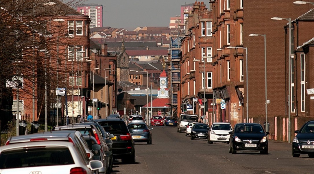 Street in the Bridgeton and Dalmarnock neighbourhood with red brick tenements on either side and cars on the road