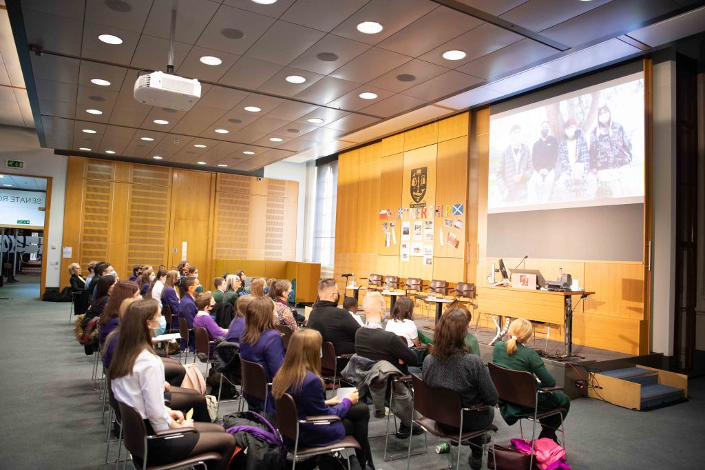 An audience sit in a lecture theatre looking at a screen showing a conference call to school pupils in Chile during COP26 climate summit